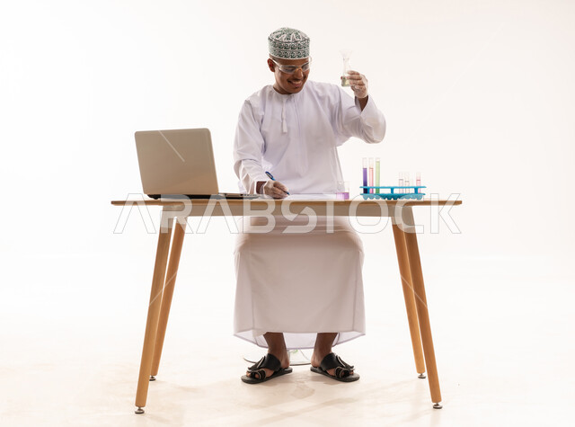 باحث عُماني يعمل على كمبيوتر محمول وقارورة مخبرية