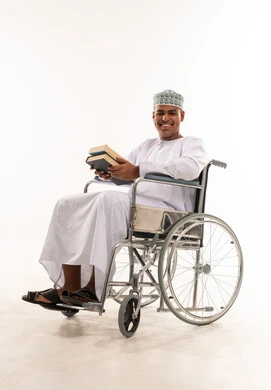 رجل عماني على كرسي متحرك يحمل كتباً
