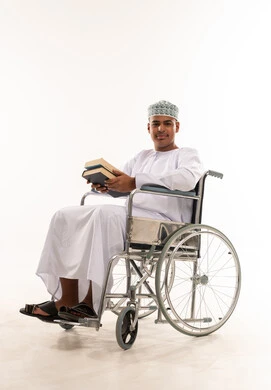 شاب عُماني على كرسي متحرك يحمل كتباً في الاستوديو