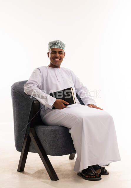 رجل عماني بالزي التقليدي يمسك كتاباً