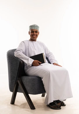 رجل عماني بالزي التقليدي يمسك كتاباً