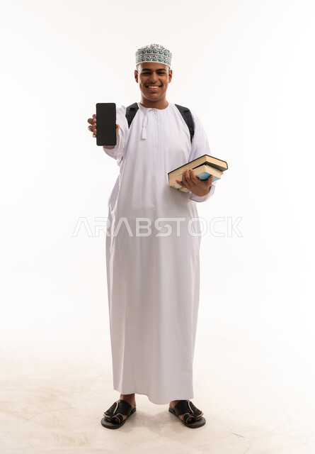 طالب عماني يحمل هاتف ذكي وكتب دراسية