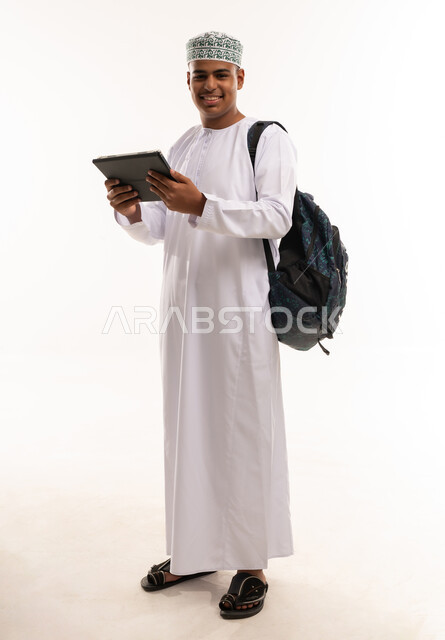طالب عماني يحمل جهازا لوحيا وحقيبة ظهر بخلفية بيضاء