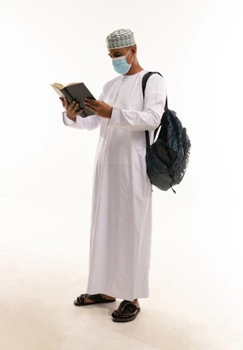 طالب عماني يقرأ كتاباً ويرتدي كمامة طبية أمام خلفية بيضاء