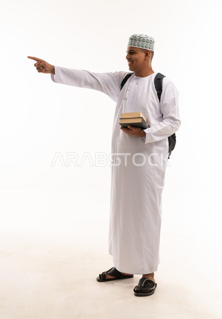 طالب عماني يحمل كتباً ويشير على خلفية بيضاء