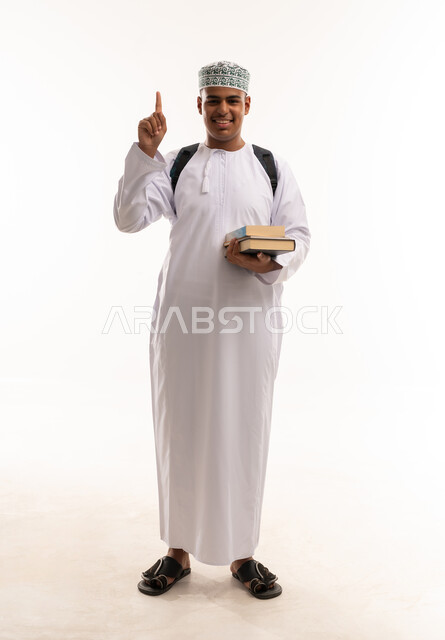 طالب عماني يحمل كتباً ويشير للأعلى