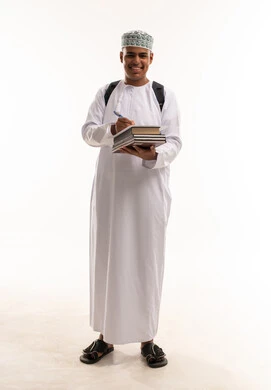 طالب عُماني يحمل كتباً بالزي التقليدي العُماني
