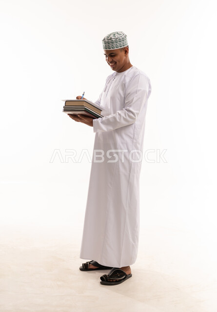رجل عماني بالزي التقليدي يكتب على الكتب