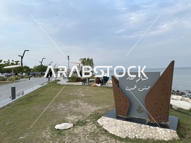 A modern walking experience, the entrance to the Hams walkway in the Eastern Province, Saudi Arabia, an open recreational destination, spaces for walking and relaxation, outdoor seating and benches, diverse restaurants and cafes, a calm family atmosphere.