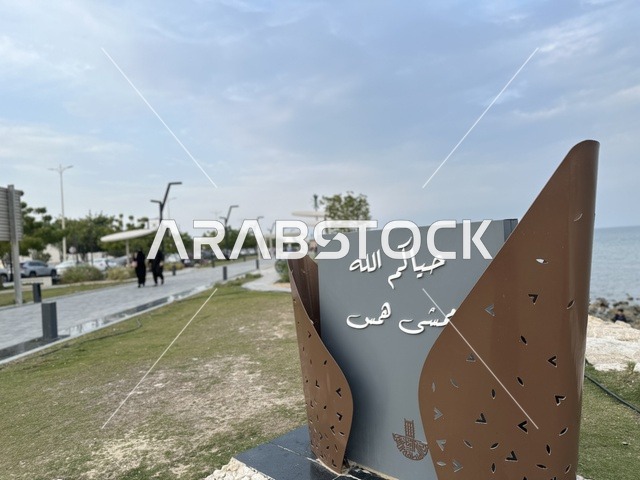 A modern walking experience, the entrance to the Hams walkway in the Eastern Province, Saudi Arabia, an open recreational destination, spaces for walking and relaxation, outdoor seating and benches, diverse restaurants and cafes, a calm family atmosphere.