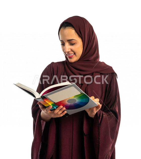 بورتريه طالبة جامعية عربية سعودية خليجية تحمل كتاب التخصص الجامعي , تخصص تصميم داخلي , تصفح وقراءة الكتب الجامعية , التعليم في جامعات المملكة العربية السعودية , خلفية بيضاء .