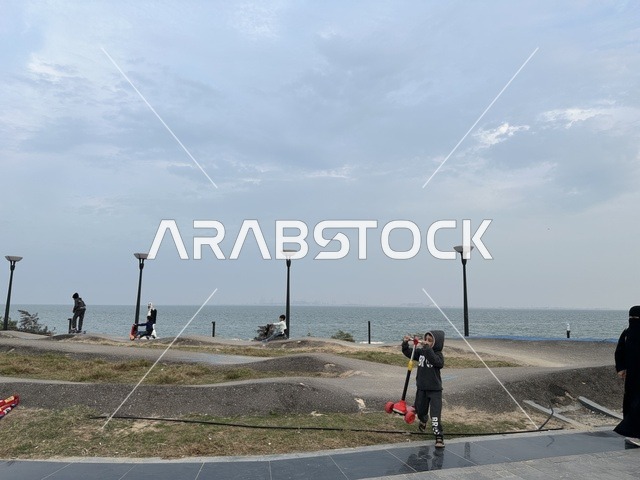 Various sports in the Hams Walkway in the Eastern Province, Saudi Arabia, a calm family atmosphere, spaces for walking and relaxation, an open recreational destination, a modern strolling experience, outdoor seating and benches.