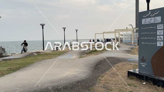 Various sports in the Hams Walkway in the Eastern Province, Saudi Arabia, a calm family atmosphere, spaces for walking and relaxation, an open recreational destination, a modern strolling experience, outdoor seating and benches.