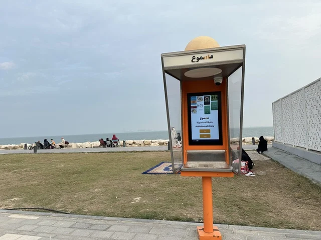 The audio library cabins "Masmoo" in the Hams Walkway in the Eastern Province, Saudi Arabia, offer a calm family atmosphere, walking and relaxation spaces, an open entertainment destination, a modern strolling experience, and outdoor seating and benches.