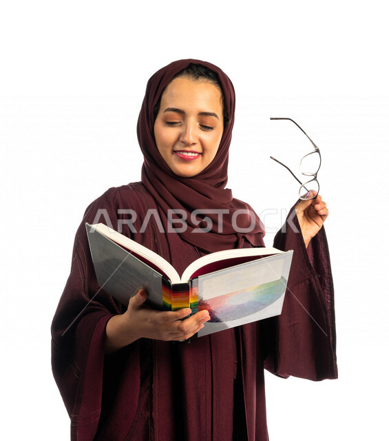 بورتريه طالبة جامعية عربية سعودية خليجية تحمل كتاب التخصص الجامعي , تخصص تصميم داخلي , تصفح وقراءة الكتب الجامعية , التعليم في جامعات المملكة العربية السعودية , خلفية بيضاء .