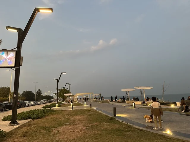 The lights and street lamps at night in the Hams Walkway in the Eastern Province, Saudi Arabia, create a calm family atmosphere, a modern strolling experience, an open entertainment destination, spaces for walking and relaxation, and outdoor seating and benches.