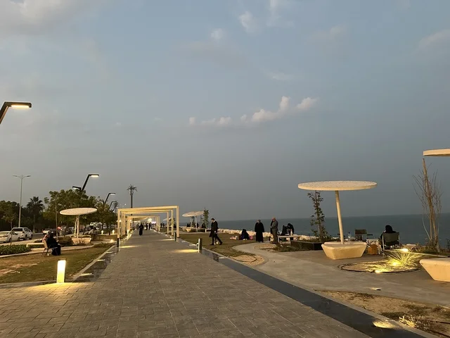 The lights and street lamps at night in the Hams Walkway in the Eastern Province, Saudi Arabia, create a calm family atmosphere, a modern strolling experience, an open entertainment destination, spaces for walking and relaxation, and outdoor seating and benches.