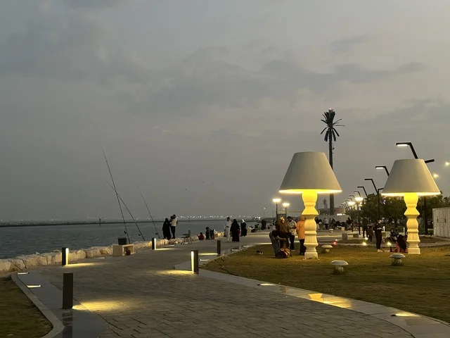 The lights and street lamps at night in the Hams Walkway in the Eastern Province, Saudi Arabia, create a calm family atmosphere, a modern strolling experience, an open entertainment destination, spaces for walking and relaxation, and outdoor seating and benches.