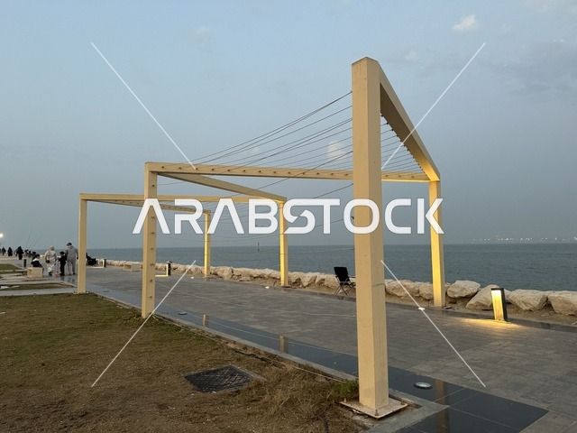 Walking and relaxation areas in the Hams Walkway in the Eastern Province, Saudi Arabia, a calm family atmosphere, a modern strolling experience, an open entertainment destination, outdoor seating and benches.