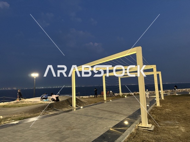 Walking and relaxation areas in the Hams Walkway in the Eastern Province, Saudi Arabia, a calm family atmosphere, a modern strolling experience, an open entertainment destination, outdoor seating and benches.