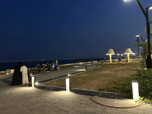 Hams Walk in the Eastern Province at night, Saudi Arabia, a calm family atmosphere, a modern walking experience, an open entertainment destination, spaces for walking and relaxation, outdoor seating and benches.