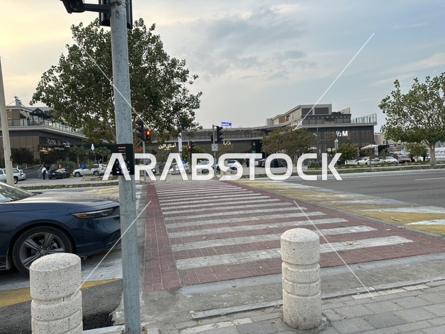 Pedestrian and vehicle crossing at the Hams walkway in the Eastern Province at night, Saudi Arabia, a calm family atmosphere, a modern strolling experience, an open entertainment destination, spaces for walking and relaxing, outdoor seating and benches.
