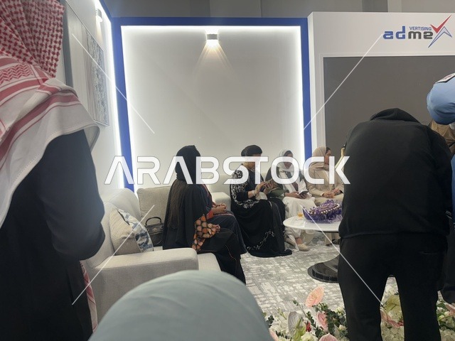 Communication through modern technological devices, gathering visitors at the Designers' Exhibition in the Eastern Province on December 29, 2025, Saudi Arabia, highlighting identity and innovation, direct interaction with visitors, a creative platform for fashion and design, and an elegant atmosphere inside the exhibition.