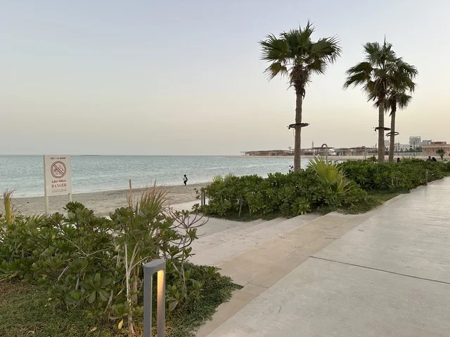 رصيف مشي حديث يمتد على طول الشاطئ، سولت البحر وجهة ترفيهية وشاطئية عائلية تقع على طريق الكورنيش في الخبر في المملكة العربية السعودية، تجديدات إضافية وتطويرات في 3  يناير 2026، شاطئ رملي مع وجود مظلات وأشجار نخيل