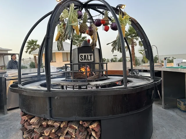 جهاز شواء دائري يستخدم في الفعاليات والمطاعم، سولت البحر وجهة ترفيهية وشاطئية عائلية تقع على طريق الكورنيش في الخبر في المملكة العربية السعودية، تجديدات إضافية وتطويرات في 3  يناير 2026، شاطئ رملي مع وجود مظلات وأشجار نخيل