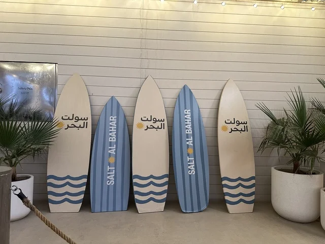 ألواح ركوب الأمواج المعروضة في مكان ما، سولت البحر وجهة ترفيهية وشاطئية عائلية تقع على طريق الكورنيش في الخبر في المملكة العربية السعودية، تجديدات إضافية وتطويرات في 3  يناير 2026، شاطئ رملي مع وجود مظلات وأشجار نخيل