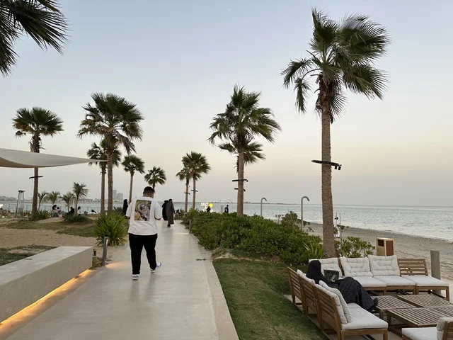 رصيف مشي حديث يمتد على طول الشاطئ، سولت البحر وجهة ترفيهية وشاطئية عائلية تقع على طريق الكورنيش في الخبر في المملكة العربية السعودية، تجديدات إضافية وتطويرات في 3  يناير 2026، شاطئ رملي مع وجود مظلات وأشجار نخيل