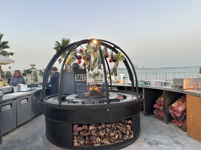 جهاز شواء دائري يستخدم في الفعاليات والمطاعم، سولت البحر وجهة ترفيهية وشاطئية عائلية تقع على طريق الكورنيش في الخبر في المملكة العربية السعودية، تجديدات إضافية وتطويرات في 3  يناير 2026، شاطئ رملي مع وجود مظلات وأشجار نخيل