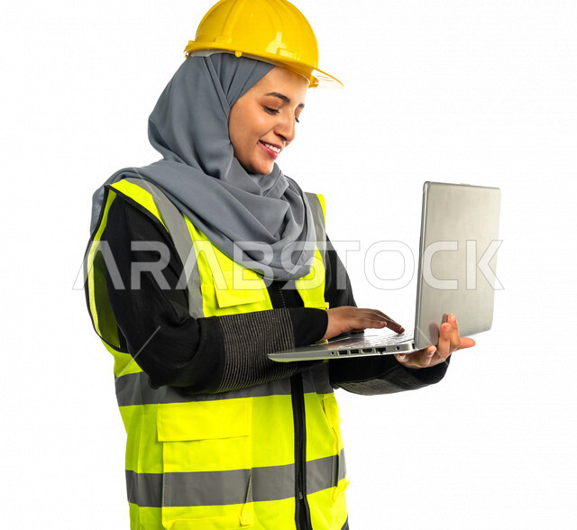بورتريه مهندسة معمارية عربية سعودية خليجية تحمل بيدها جهاز اللابتوب المحمول ، مهندسة انشاءات محجبة ترتدي بدلة السلامة في العمل ، خوذة العمل ، لباس رسمي للعمل ، مشروع بناء ، خلفية بيضاء
