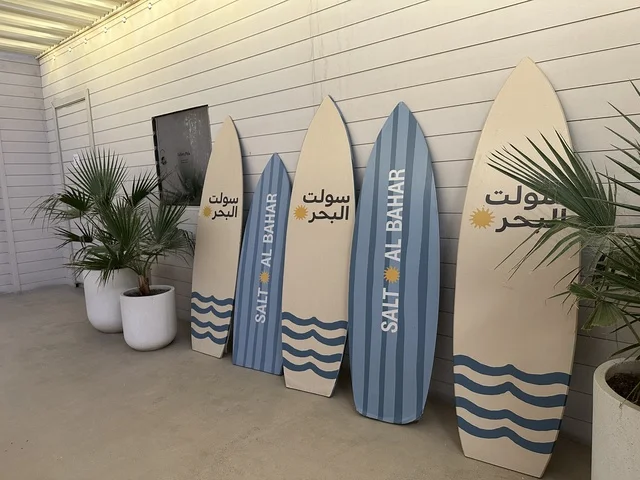 ألواح ركوب الأمواج المعروضة في مكان ما، سولت البحر وجهة ترفيهية وشاطئية عائلية تقع على طريق الكورنيش في الخبر في المملكة العربية السعودية، تجديدات إضافية وتطويرات في 3  يناير 2026، شاطئ رملي مع وجود مظلات وأشجار نخيل
