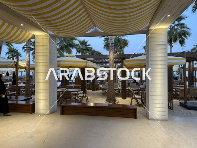 تصميم خارجي بأسقف قماشية مخططة باللونين الأصفر والأبيض، سولت البحر وجهة ترفيهية وشاطئية عائلية تقع على طريق الكورنيش في الخبر في المملكة العربية السعودية، تجديدات إضافية وتطويرات في 3  يناير 2026، شاطئ رملي مع وجود مظلات وأشجار نخيل