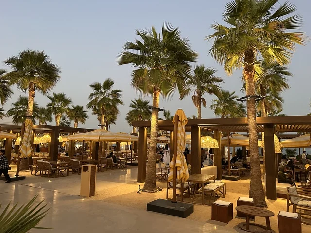 أرضية رملية في منطقة الجلوس، سولت البحر وجهة ترفيهية وشاطئية عائلية تقع على طريق الكورنيش في الخبر في المملكة العربية السعودية، تجديدات إضافية وتطويرات في 3  يناير 2026، شاطئ رملي مع وجود مظلات وأشجار نخيل