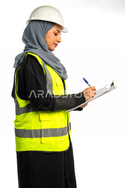 بورتريه مهندسة معمارية عربية سعودية خليجية تحمل بيدها ملف المهام والمخططات ، مهندسة انشاءات محجبة ترتدي بدلة السلامة في العمل ، خوذة العمل ، لباس رسمي للعمل ، مشروع بناء ، خلفية بيضاء