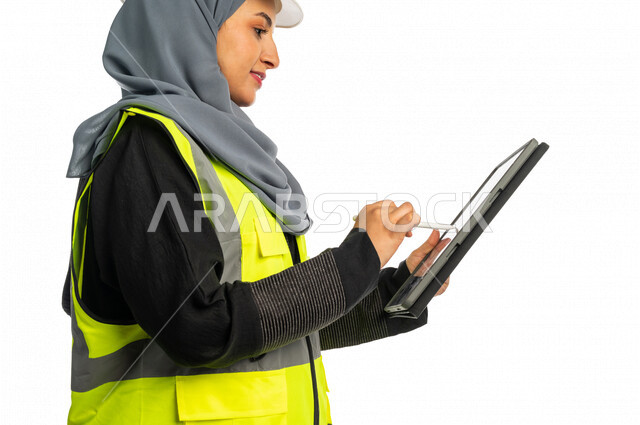 بورتريه مهندسة معمارية عربية سعودية خليجية تحمل بيدها جهاز التابلت لرؤية مخطط البناء ، مهندسة انشاءات محجبة ترتدي بدلة السلامة في العمل ، خوذة العمل ، لباس رسمي للعمل ، مشروع بناء ، خلفية بيضاء