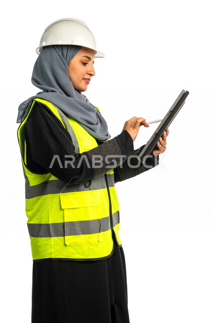بورتريه مهندسة معمارية عربية سعودية خليجية تحمل بيدها جهاز التابلت لرؤية مخطط البناء ، مهندسة انشاءات محجبة ترتدي بدلة السلامة في العمل ، خوذة العمل ، لباس رسمي للعمل ، مشروع بناء ، خلفية بيضاء