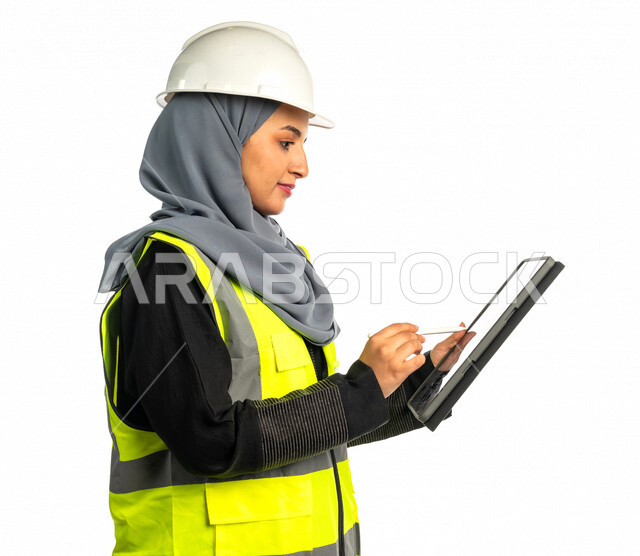 بورتريه مهندسة معمارية عربية سعودية خليجية تحمل بيدها جهاز التابلت لرؤية مخطط البناء ، مهندسة انشاءات محجبة ترتدي بدلة السلامة في العمل ، خوذة العمل ، لباس رسمي للعمل ، مشروع بناء ، خلفية بيضاء