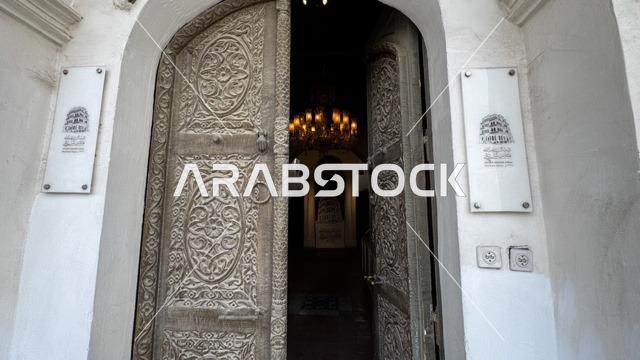 A wooden door intricately carved and decorated, architectural arts in the historic city of Jeddah, drone photography of alleys and traditional designs, tourist attractions in the Kingdom of Saudi Arabia, ancient archaeological buildings, revitalization projects in the area.