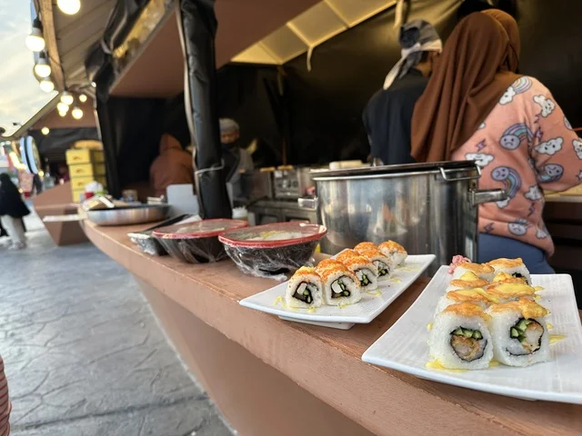 A kiosk selling Chinese food, taste a sushi dish, activate tourism and economic movement, a tourist and entertainment attraction, the global city January 2026 on the shores of the Arabian Gulf and Lake Sehat in the Eastern Province of Dammam, get to know the different cultures of the countries, a place to spend enjoyable time with family.