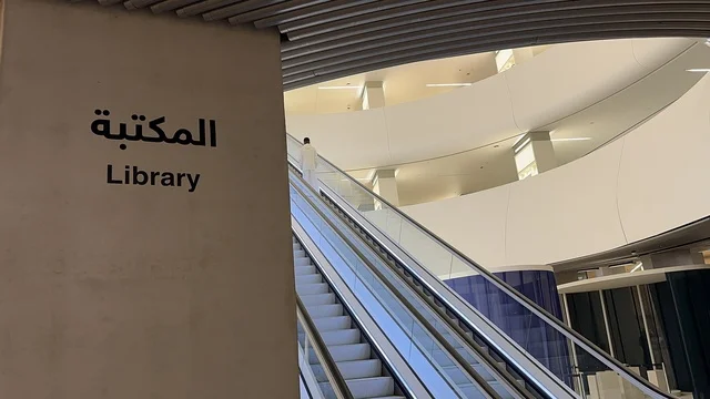 Entrance of the modern cultural building, library sign in Arabic and English, escalator inside the Ithra Center, internal corridor in a cultural building, King Abdulaziz Center for World Culture.