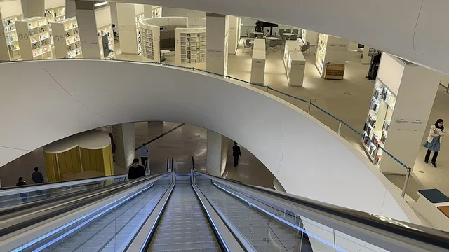 تصميم معماري داخلي حديث، سلالم كهربائية داخل مبنى ثقافي، رفوف كتب في مساحة مفتوحة، بيئة معرفية عصرية، مركز الملك عبد العزيز الثقافي العالمي، معارض ومكتبات ، اماكن ثقافية تعليمية في السعودية