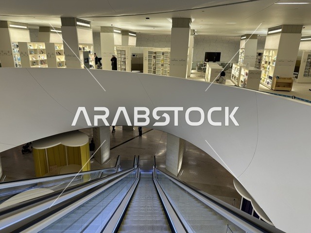 تصميم معماري داخلي حديث، سلالم كهربائية داخل مبنى ثقافي، رفوف كتب في مساحة مفتوحة، بيئة معرفية عصرية، مركز الملك عبد العزيز الثقافي العالمي، معارض ومكتبات ، اماكن ثقافية تعليمية في السعودية