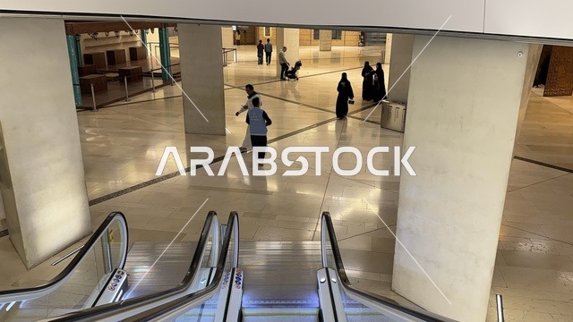 A wide internal corridor inside a modern cultural building, escalators with a contemporary design, visitor movement within the interior space, a calm atmosphere, and contemporary architectural organization, the King Abdulaziz Center for World Culture (Ithra) in Dhahran, Eastern Province, Saudi Arabia.