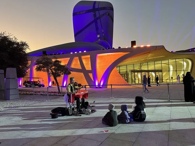 مبنى مركز الملك عبد العزيز الثقافي العالمي (إثراء) بإضاءة ليلية ملونة، تصميم معماري أيقوني، حركة الزوار في الساحة الخارجية، أجواء ثقافية وترفيهية