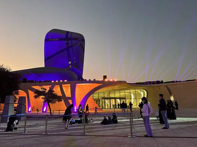مبنى مركز الملك عبد العزيز الثقافي العالمي (إثراء) بإضاءة ليلية ملونة، تصميم معماري أيقوني، حركة الزوار في الساحة الخارجية، أجواء ثقافية وترفيهية