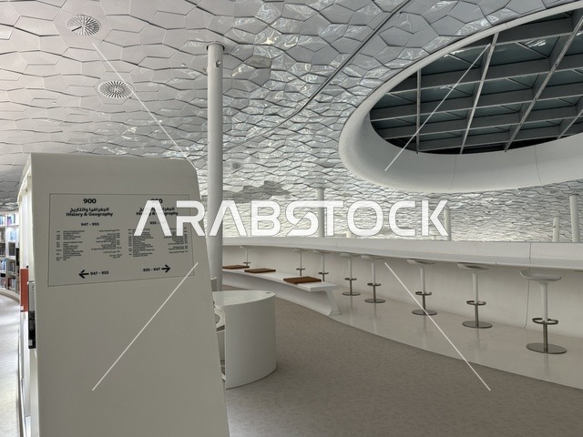 تصميم داخلي عصري لمساحة معرفية، منطقة جلوس للقراءة والدراسة، سقف معماري هندسي مبتكر، لافتات إرشادية لتنظيم الأقسام، بيئة هادئة داخل مبنى ثقافي حديث، مكتبة مركز الملك عبدالعزيز للثقافة العالمية (إثراء) في الظهران