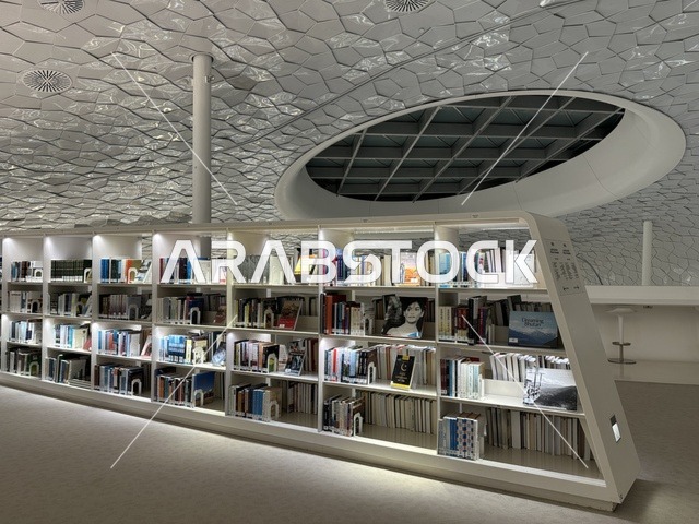 رفوف كتب منظمة داخل مساحة معرفية حديثة، تصميم داخلي عصري بإضاءة هادئة، سقف معماري هندسي مبتكر، بيئة تعليمية وثقافية داخل مبنى حديث، مكتبة مركز الملك عبدالعزيز للثقافة العالمية (إثراء) في الظهران